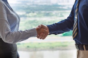 Closeup of businessman and businesswoman shaking hands with blurry city view in background. People are seen partly.